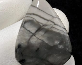 May include: A gray and white agate cabochon with a unique pattern of swirling lines and veins. The stone is smooth and polished, and it has a natural, organic look.