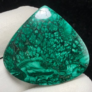 Peut inclure: Une pierre précieuse de malachite polie en forme de goutte d'eau. La pierre présente une couleur vert foncé avec des motifs complexes de veines vertes plus claires et noires. La surface est lisse et réfléchissante, mettant en valeur la beauté naturelle du minéral.