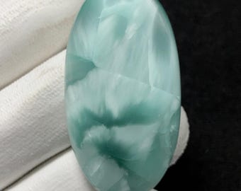 Può includere: Una gemma ovale con un motivo azzurro e bianco. La pietra lucida ha un aspetto marmorizzato, con vortici color verde acqua più scuri. La gemma è tenuta da una mano guantata di bianco.