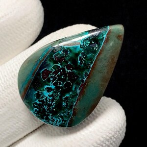 May include: A polished gemstone with a teardrop shape. The stone features a mix of teal, turquoise, and brown colors. The teal and turquoise areas have a textured, almost crystalline appearance, while the brown sections have a smooth finish.