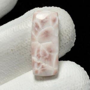 May include: A white and pink cabochon gemstone with a unique, organic pattern. The stone is rectangular in shape and has a smooth, polished surface.