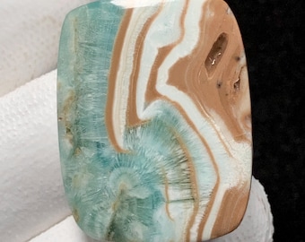 May include: A rectangular gemstone with rounded edges, displaying a mix of colours. The stone features light blue, white, and brown hues, arranged in a swirling pattern. The surface of the gemstone is smooth and polished.