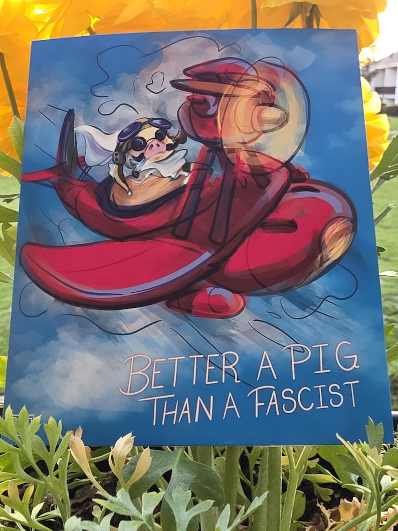 May include: A blue print featuring a cartoon pig wearing goggles and a scarf, flying a red airplane against a cloudy sky. The text "BETTER A PIG THAN A FASCIST" is written in white cursive.