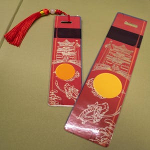 May include: Two red rectangular decorative items with gold accents, featuring a pagoda design and a yellow circle. One has a red tassel. The items have a dragon illustration and a black band.