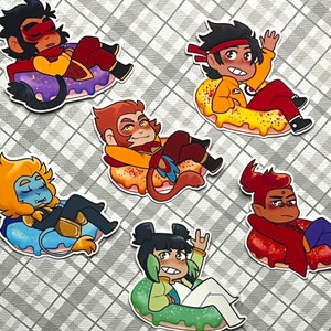 以下が含まれることがあります： ドーナツの形をしたステッカーに、カラフルな漫画のキャラクターが5人描かれています。それぞれのキャラクターは異なる服装をし、ユニークな表情をしています。キャラクターはそれぞれ異なるポーズをとっており、座っているものもいれば、立っているものもいれば、横になっているものもいます。ドーナツはすべて異なる色で、スプリンクルがかけられています。