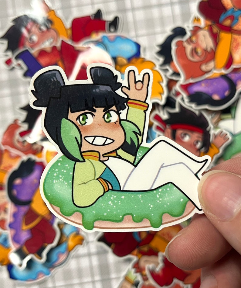 以下が含まれることがあります： 緑と白のドーナツのステッカーに、漫画のキャラクターが座っています。キャラクターは黒髪で緑色の目で、緑と黄色のシャツを着ています。キャラクターは右手でピースサインをしています。