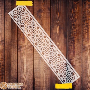 May include: White stencil with a repeating geometric pattern of circles and ovals. The stencil is taped to a wooden surface.