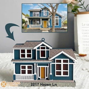 Op de afbeelding: Een blauw huis ornament met witte versiering en een bruin dak. Het ornament heeft een wit balkon met witte leuningen en een bruine deur. Het ornament heeft het adres "2217 Hazen Ln" op de basis gedrukt.