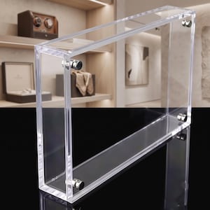 May include: A rectangular clear acrylic display frame featuring two thick transparent panels held together by four small silver-toned metal cylindrical fasteners at each corner, designed for showcasing flat items in a vertical orientation.