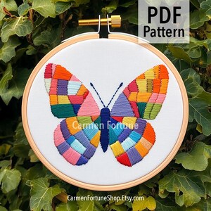 May include: A colorful butterfly embroidery pattern on white fabric, set in a wooden hoop. The butterfly design features a patchwork of vibrant colors, including orange, yellow, pink, and blue. The text "PDF Pattern" is in the upper right corner.