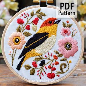 May include: Embroidered bird and floral design in a wooden hoop. The bird features orange, yellow, black, and white thread. Pink and peach flowers and red berries surround the bird. The text "PDF Pattern" is in the upper right corner.