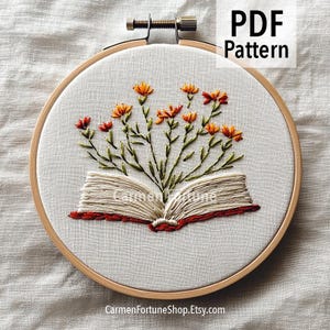 May include: Embroidered hoop art showing an open book with orange and red flowers. The embroidery is on white fabric, set in a wooden hoop. The text "PDF Pattern" is in the upper right corner. The shop name is at the bottom.
