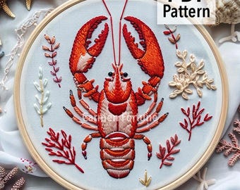 May include: Embroidered lobster design in a wooden hoop. The lobster is red and orange, surrounded by embroidered seaweed and the text "PDF Pattern". The background is a light blue fabric. The Etsy shop name is visible.