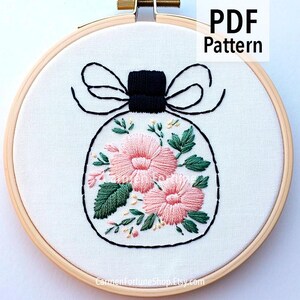 Puede incluir: Diseño floral bordado en un aro de madera. El diseño presenta una forma de botella de perfume con flores rosas, hojas verdes y un lazo negro. El texto "PDF Pattern" es visible en la esquina superior derecha.