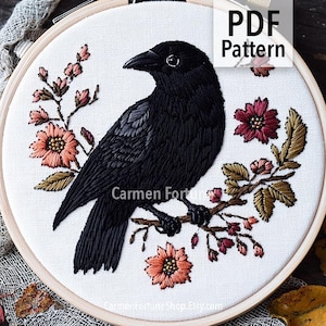 May include: Embroidered crow design in a wooden hoop. The black crow is perched on a branch with peach and burgundy flowers and green leaves. The text "PDF Pattern" is in the upper right corner.