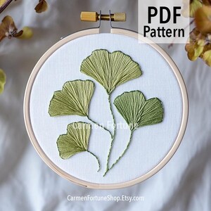 May include: An embroidery hoop featuring a green ginkgo leaf design. The leaves are stitched on white fabric, with the text "PDF Pattern" in the upper right corner. The shop name, CarmenFortuneShop.Etsy.com, is at the bottom.