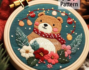Könnte beinhalten: Gesticktes Stickrahmen-Kunstwerk mit einem braunen Bären mit rotem Schal, umgeben von Blumen und Grün. Der Bär ist auf teal-farbenem Stoff gestickt, mit dem Text "PDF Pattern". Der Holzrahmen ist sichtbar.