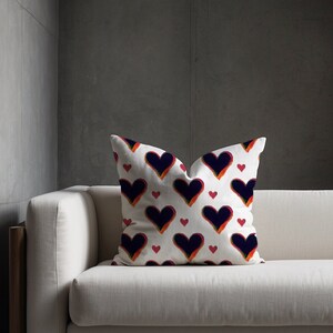 Könnte beinhalten: Ein weißes Sofa mit einem Kissen mit einem sich wiederholenden Muster aus schwarzen, roten und orangefarbenen Herzen. Das Sofa steht in einem modernen Wohnzimmer mit grauen Wänden.