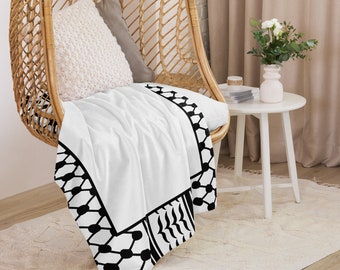 May include: A white throw blanket with a black and white geometric pattern border. The blanket is draped over a wicker chair with a white pillow.