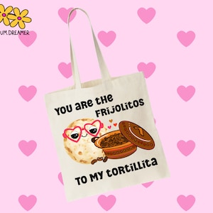 May include: A white tote bag with a cartoon illustration of a tortilla with heart-shaped sunglasses and a pot of frijoles. The text on the bag reads "You are the Frijolitos to my Tortillita."