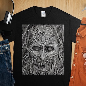 May include: Black t-shirt with a graphic print of a detailed, monstrous face with vines growing from its head. The face has a menacing expression with sharp teeth and a wide, open mouth.