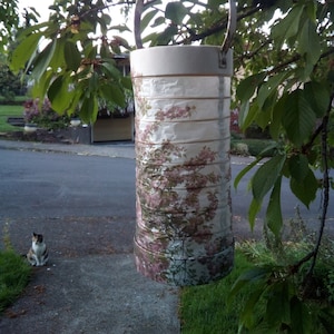 以下が含まれることがあります： 木の枝にぶら下がっている、花柄の白い紙提灯。提灯は金属製の取っ手があり、複数の紙の層でできています。