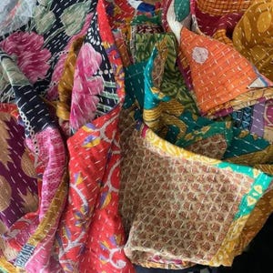 May include: A multi-colored textile quilt featuring a patchwork of various fabrics with floral, geometric, and abstract patterns. The fabric pieces are joined together with visible white running stitch embroidery throughout the entire surface.