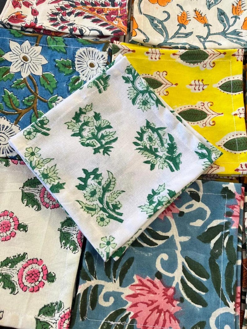 K&ouml;nnte beinhalten: Eine Sammlung gefalteter Stoffservietten mit verschiedenen floralen Mustern. Die Servietten zeigen Designs in Gr&uuml;n, Rosa, Blau, Gelb und Wei&szlig;. Die Muster umfassen stilisierte Blumen und botanische Motive, f&uuml;r die Inneneinrichtung.