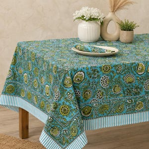 May include: A rectangular tablecloth featuring a vibrant turquoise background with a repeating floral pattern in shades of olive green, dark brown, and white. The edges are finished with a distinct white and turquoise striped border design.