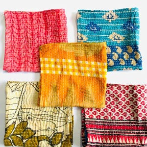 May include: Five square fabric pieces featuring kantha stitching. The collection includes a pink textured piece, a teal floral print, a yellow and white checkered square, a cream piece with olive leaf patterns, and a red and white geometric print.