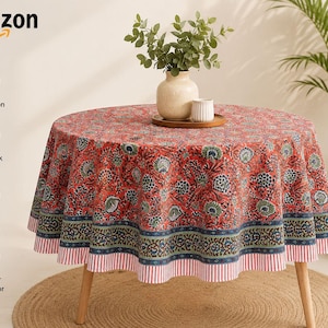 Puede incluir: Un mantel redondo con base roja y un patrón floral repetitivo en azul y verde, acabado con un borde azul oscuro y un remate a rayas rojas y blancas. La tela es 100% algodón, estampada a mano con bloques y lavable a máquina.