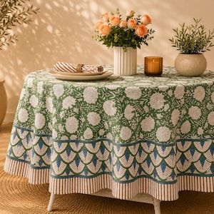 May include: A round tablecloth featuring a green and white floral pattern on the top, with a border of blue and green scalloped shapes and a brown and white striped edge. The fabric drapes over a round table, creating a decorative table covering.