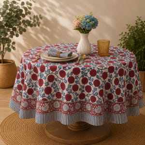 Pu&ograve; includere: Una tovaglia rotonda caratterizzata da un motivo ripetuto di fiori rosso scuro e foglie blu su sfondo bianco, con un'ampia bordura di complessi motivi floreali e strisce verticali blu e bianche lungo il bordo inferiore del tessuto.
