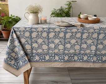 Può includere: Una tovaglia rettangolare caratterizzata da un motivo floreale stampato in blu e beige con una disposizione a griglia. Il tessuto presenta un bordo ampio con un motivo floreale più piccolo e un sottile bordo a righe. Il design copre l'intera superficie.