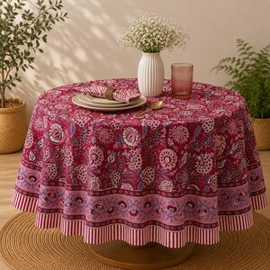 Pu&ograve; includere: Una tovaglia rotonda con una base magenta intenso e un motivo floreale ripetuto in tonalit&agrave; rosa, bianco e blu. Il bordo presenta una distinta fascia floreale rosa e una finitura a righe rosse e bianche su un tavolo circolare.