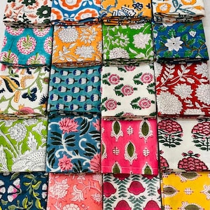 K&ouml;nnte beinhalten: Eine Sammlung gefalteter Stoffquadrate mit verschiedenen floralen Mustern. Die Designs weisen eine Reihe von Farben auf, darunter Blau, Orange, Gr&uuml;n, Rosa und Gelb. Jedes Quadrat zeigt einen einzigartigen botanischen Druck und erzeugt eine lebendige und vielf&auml;ltige Darstellung.