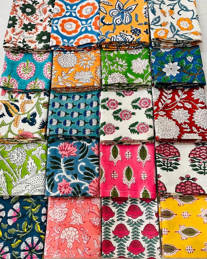K&ouml;nnte beinhalten: Eine Sammlung gefalteter Stoffquadrate mit verschiedenen floralen Mustern. Die Designs weisen eine Reihe von Farben auf, darunter Blau, Orange, Gr&uuml;n, Rosa und Gelb. Jedes Quadrat zeigt einen einzigartigen botanischen Druck und erzeugt eine lebendige und vielf&auml;ltige Darstellung.