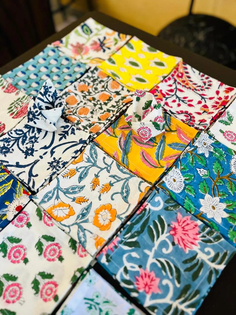 K&ouml;nnte beinhalten: Eine Sammlung bunter Stoffservietten mit floralen Mustern. Die Servietten zeigen verschiedene Designs, darunter rosa, orange und blaue Blumen, die in einem Raster angeordnet sind. Einige Servietten sind gefaltet, um ihre Muster zu zeigen.