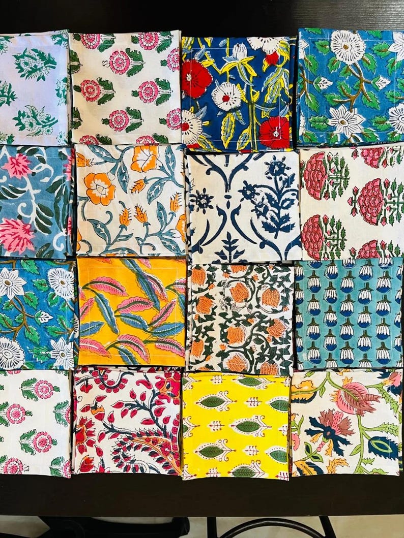 K&ouml;nnte beinhalten: Eine Sammlung von f&uuml;nfundzwanzig quadratischen Stoffuntersetzern mit verschiedenen floralen und botanischen Mustern. Die Untersetzer weisen eine Reihe von Farben auf, darunter Blau, Rot, Gelb und Gr&uuml;n, mit wei&szlig;en Hintergr&uuml;nden. Jeder Untersetzer hat ein einzigartiges Design.