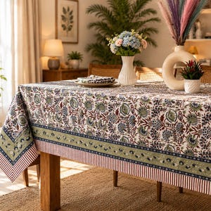 May include: A rectangular tablecloth featuring a repeating floral pattern in shades of green, blue, and maroon on a white background. The border includes a wide olive green band with small floral motifs and a thin red and white striped edge.