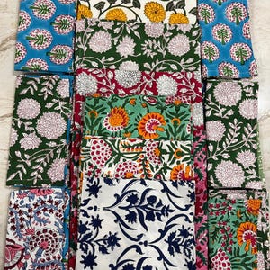 Puede incluir: Una colección de servilletas de tela rectangulares con varios patrones florales estampados en bloque. Los diseños incluyen flores amarillas, blancas y rosas sobre fondos verdes, azules y blancos, con algunos motivos botánicos azul oscuro sobre blanco.