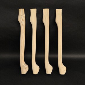 Könnte beinhalten: Vier unfertige Holzmöbelfüße mit geschwungenem Design. Die Beine sind aus hellfarbenem Holz gefertigt und haben eine glatte, natürliche Oberfläche. Die Beine sind etwa 61 cm lang.