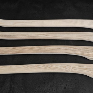 Può includere: Quattro manici di ascia in legno non finiti, tutti dello stesso stile, disposti in fila su una superficie nera.