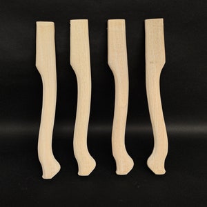 Könnte beinhalten: Vier unfertige Holzstuhlbeine mit einem geschwungenen Design.