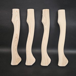 Può includere: Quattro manici di ascia in legno non rifiniti con un motivo a venature chiare. I manici hanno un design curvo e sono pronti per l'uso. I manici di ascia sono esposti su uno sfondo scuro.