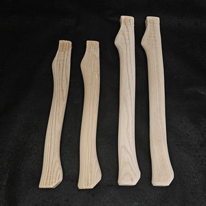 Könnte beinhalten: Vier unfertige Axt-Stiele aus Holz. Die Stiele haben alle die gleiche Form und Größe, aber unterschiedliche Längen. Die Stiele sind aus hellem Holz.