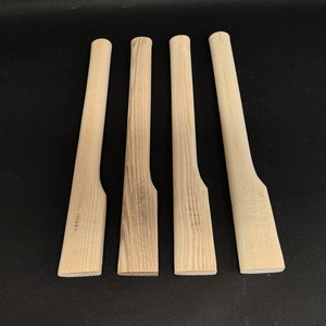 Può includere: Quattro manici di ascia in legno non finiti, ognuno con un motivo a venature leggermente diverso. I manici sono tutti lunghi circa 46 cm e hanno un'estremità arrotondata.