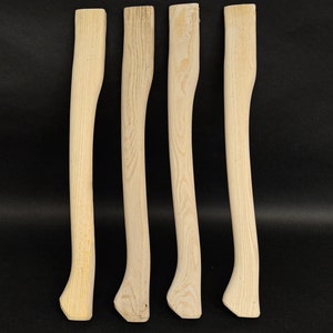 Könnte beinhalten: Vier unfertige Axt-Stiele aus Holz, alle gleich groß und in der gleichen Form, sind auf einem schwarzen Hintergrund aufgereiht.