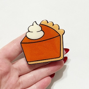 May include: A pumpkin pie slice with whipped cream, featuring orange and tan colors. The pie has a black outline and a decorative crust. A festive, food-themed item.