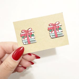 May include: A pair of book-shaped earrings with a red bow on top. The books are stacked and have a green, white, and red pattern.